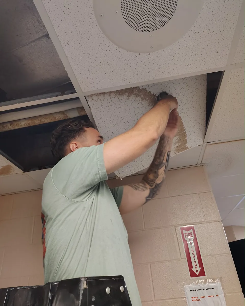 Justin replacing a water-damaged ceiling tile in a commercial building