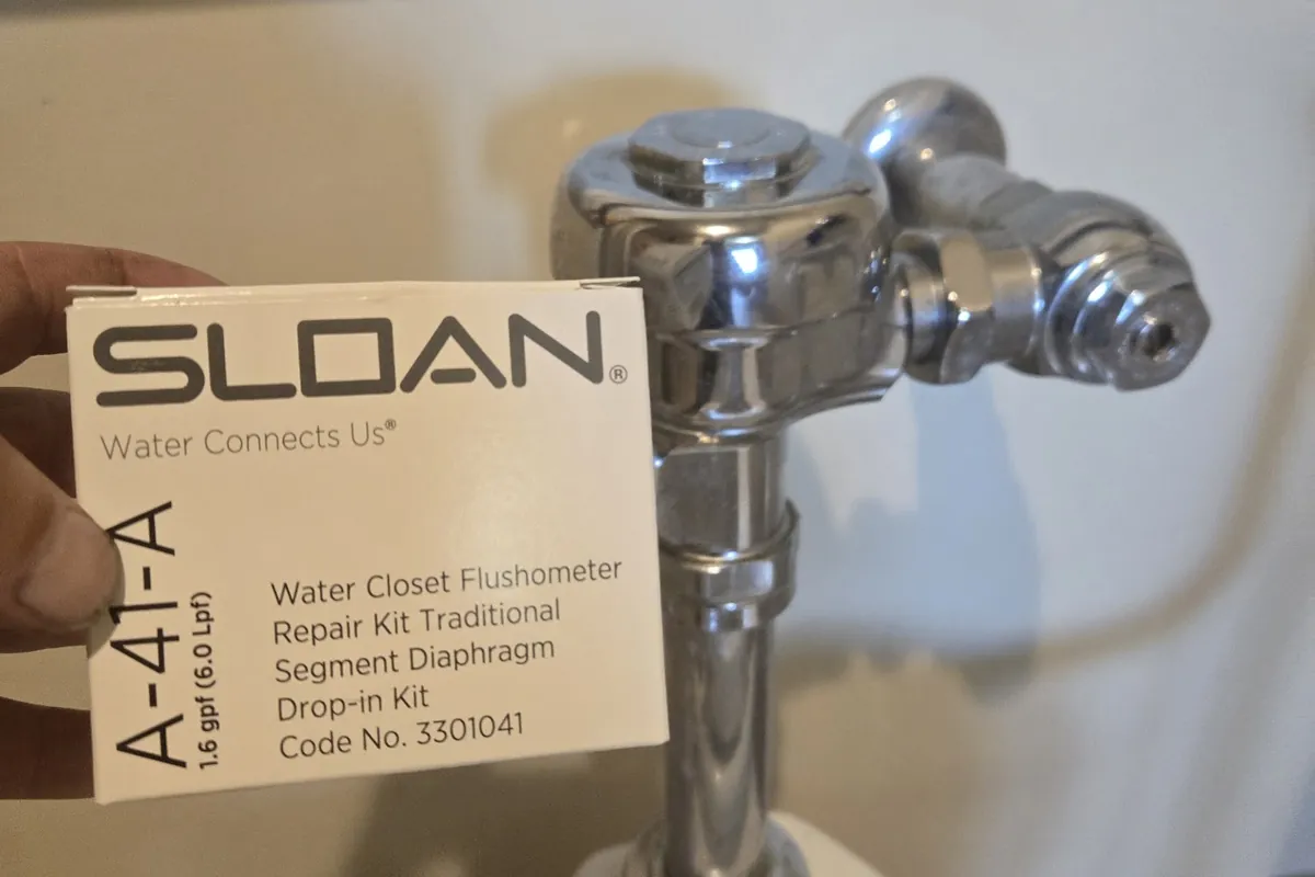 Sloan flushometer repair kit next to a commercial toilet flush valve