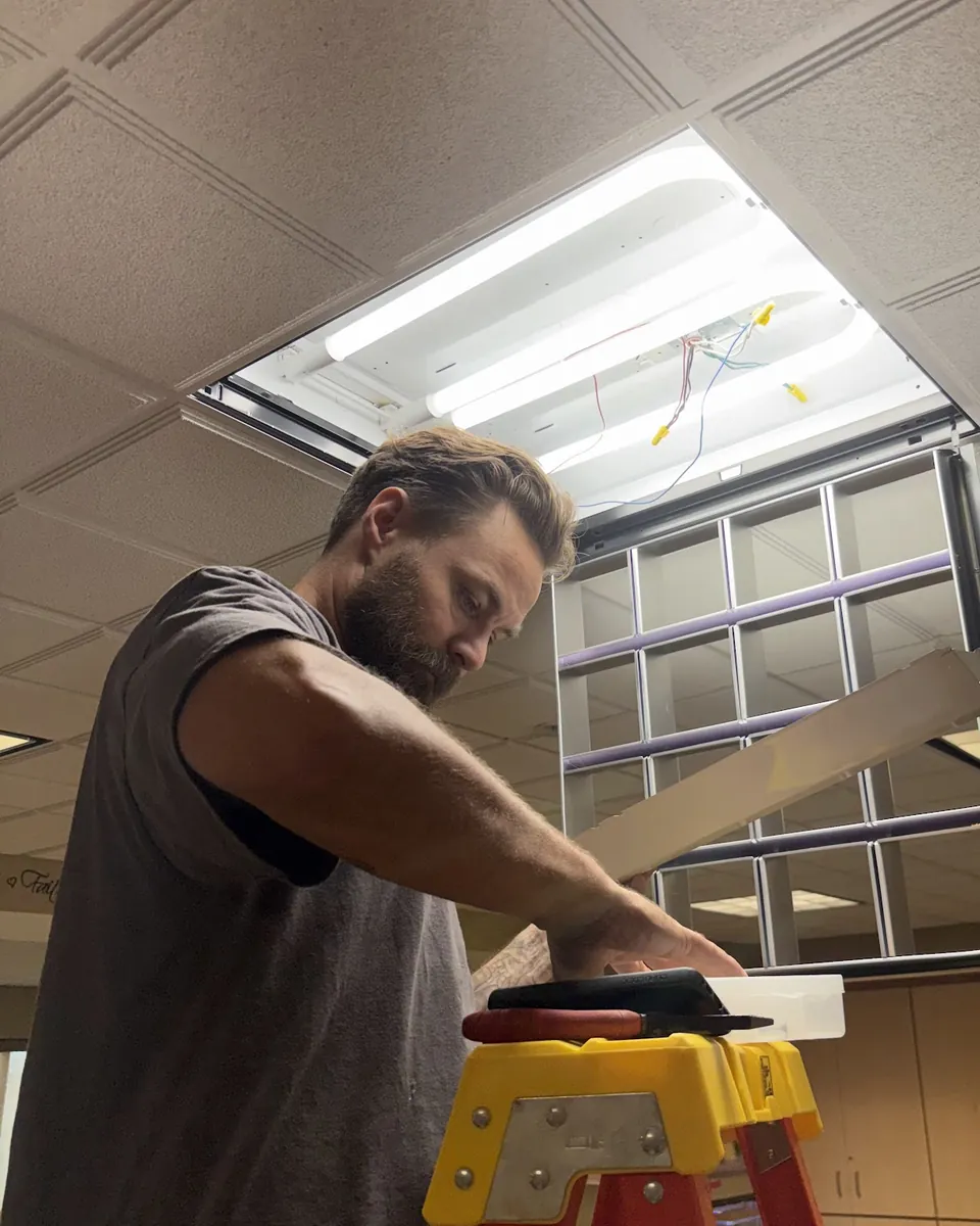 Justin of Brown's Maintenance on a ladder replacing an office ceiling light