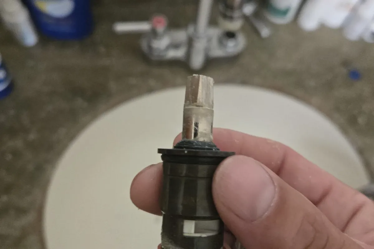 Replacement faucet cartridge held above a bathroom sink