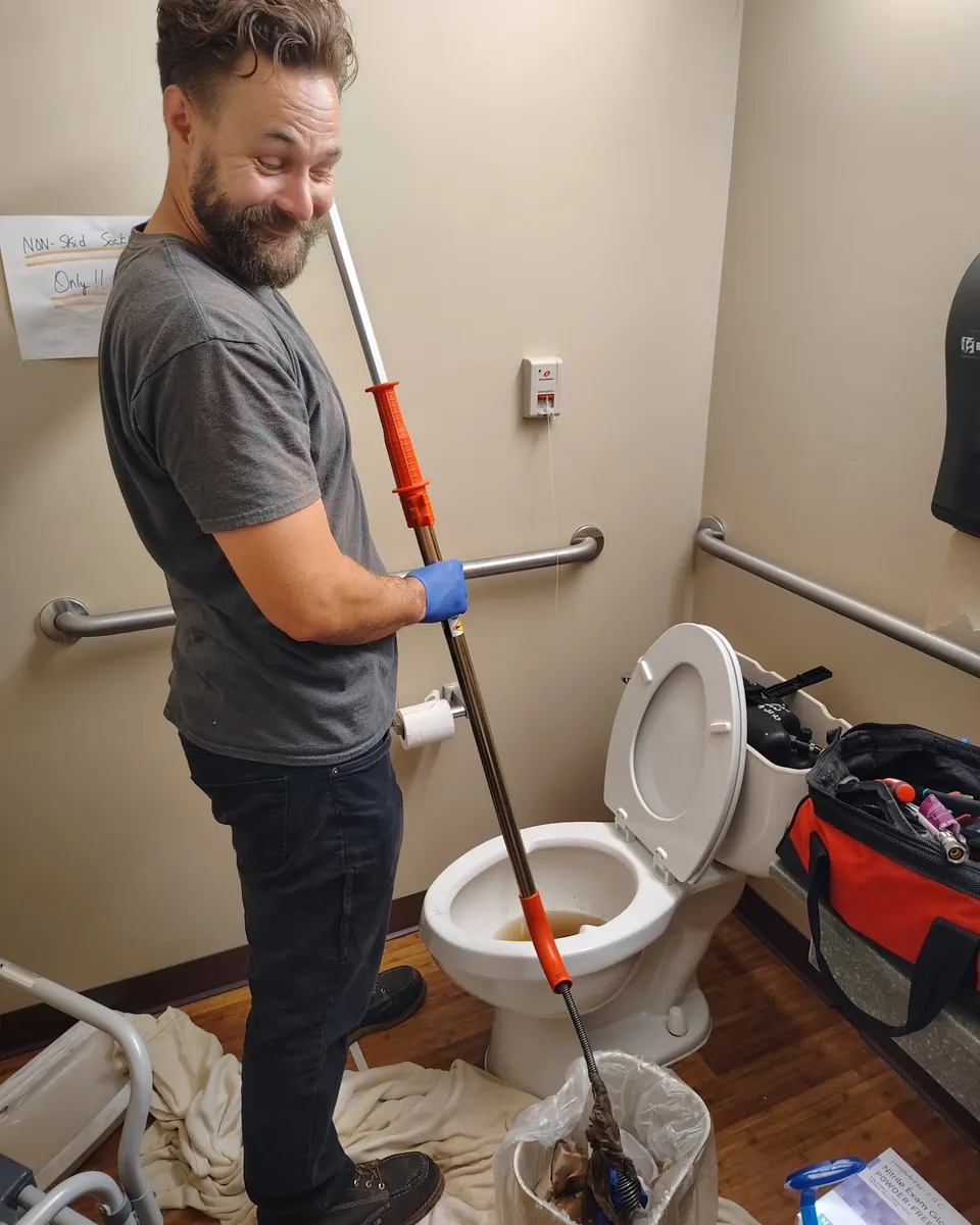 Justin clearing a clogged toilet with a drain auger