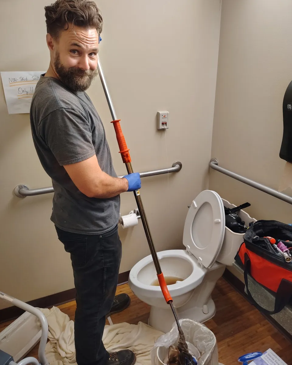 Justin clearing a toilet clog with a drain auger