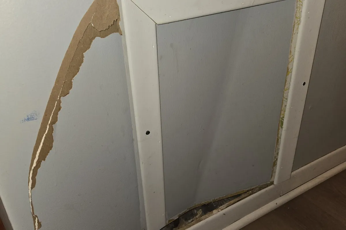 Damaged trim and torn drywall facing around a wall panel, before repair