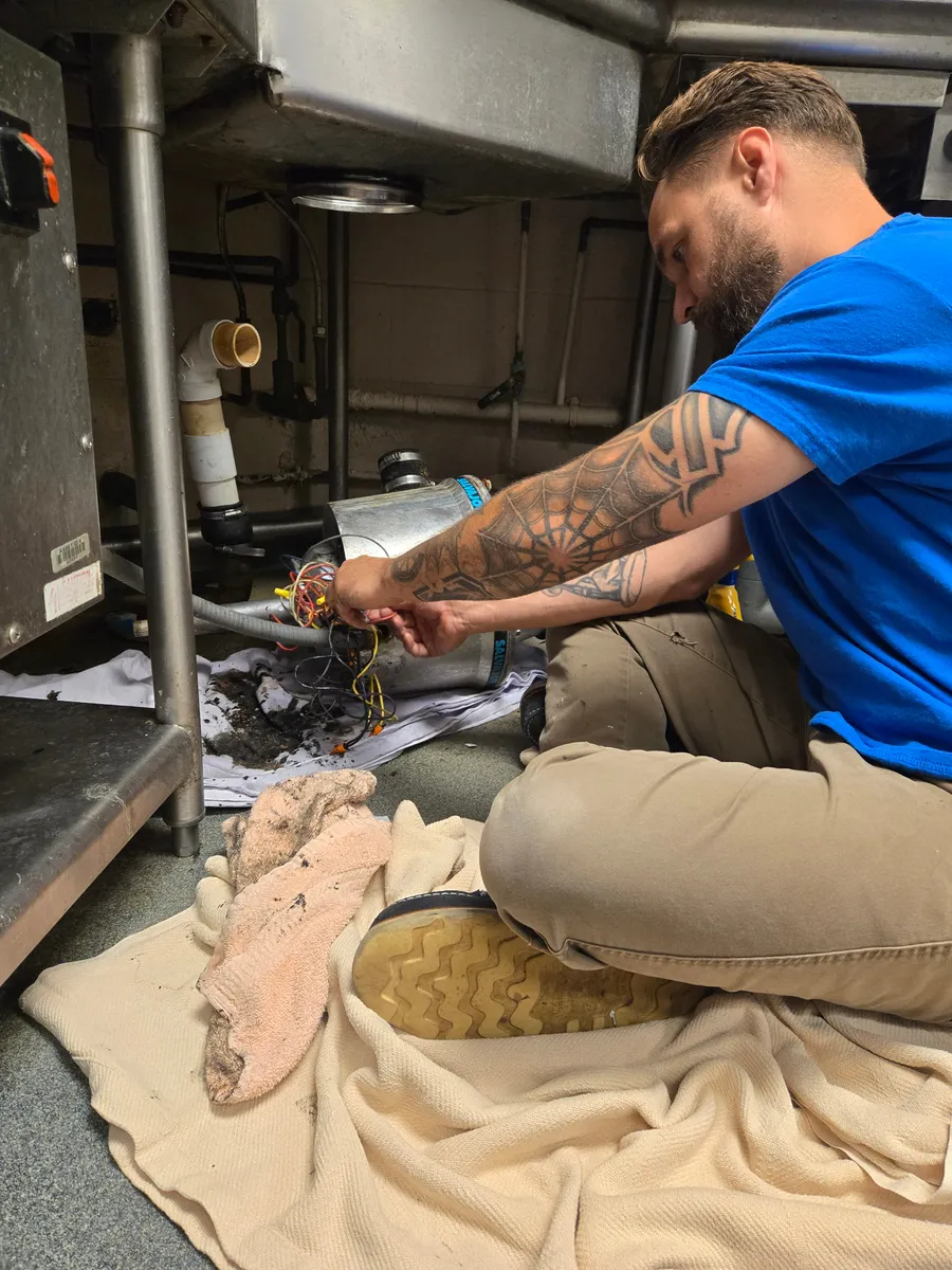 Justin working under a kitchen sink on a plumbing fixture repair